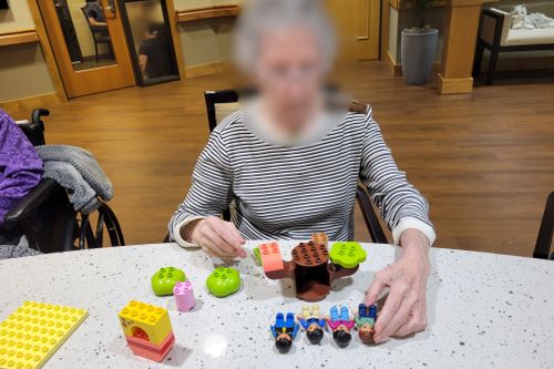 Blurred senior holding LEGO® brick people and creating