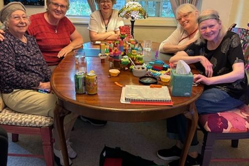 Natalia with seniors as they smile into the camera with their work on a wooden oval dining table